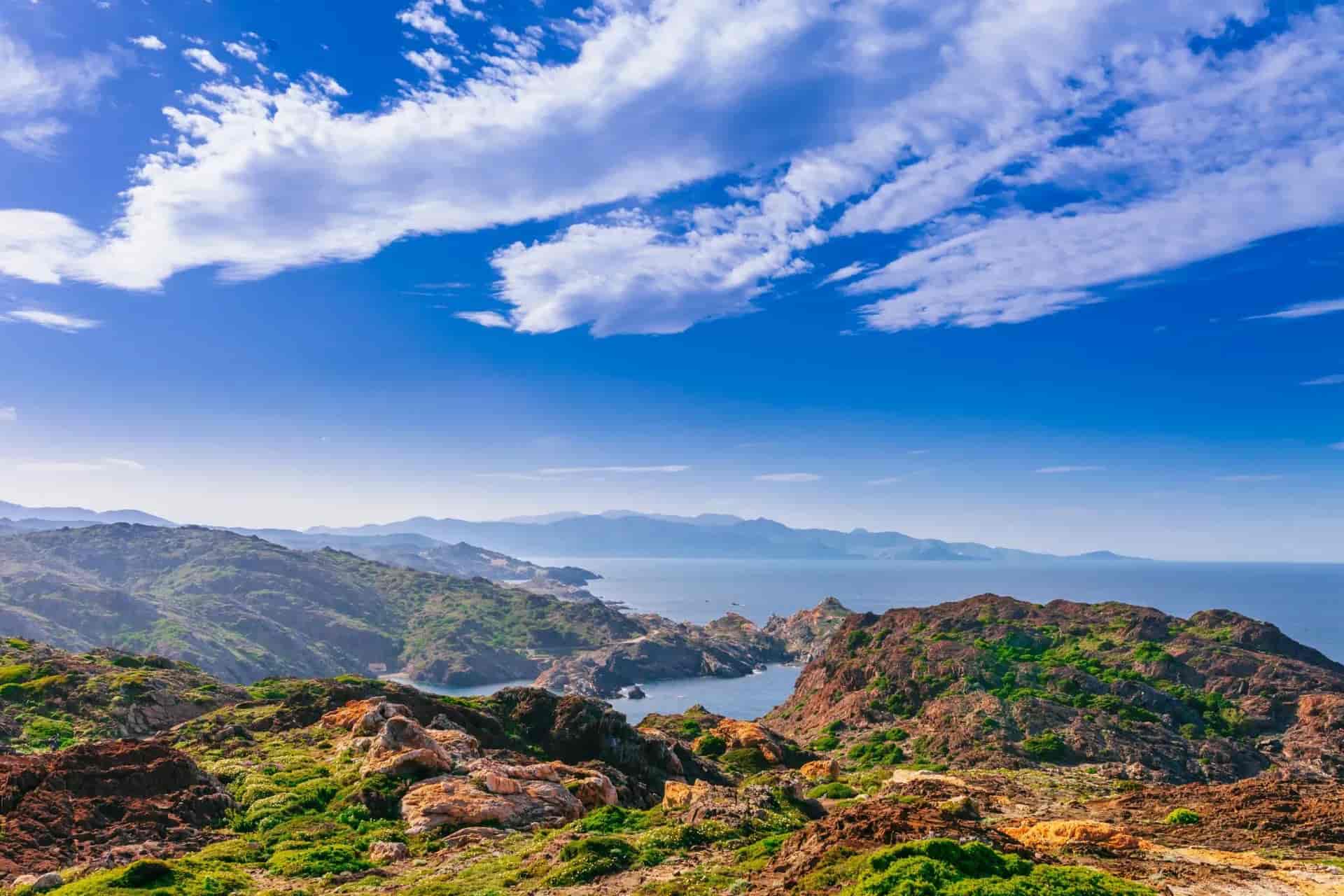 Rocky Cap de Creus coastline overlooking the Mediterranean Sea under a blue sky with white clouds.