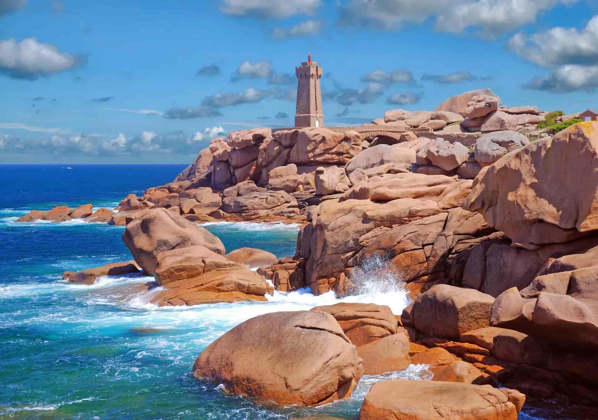 Ploumanac'h Lighthouse atop pink granite rocks above turquoise sea under blue sky.