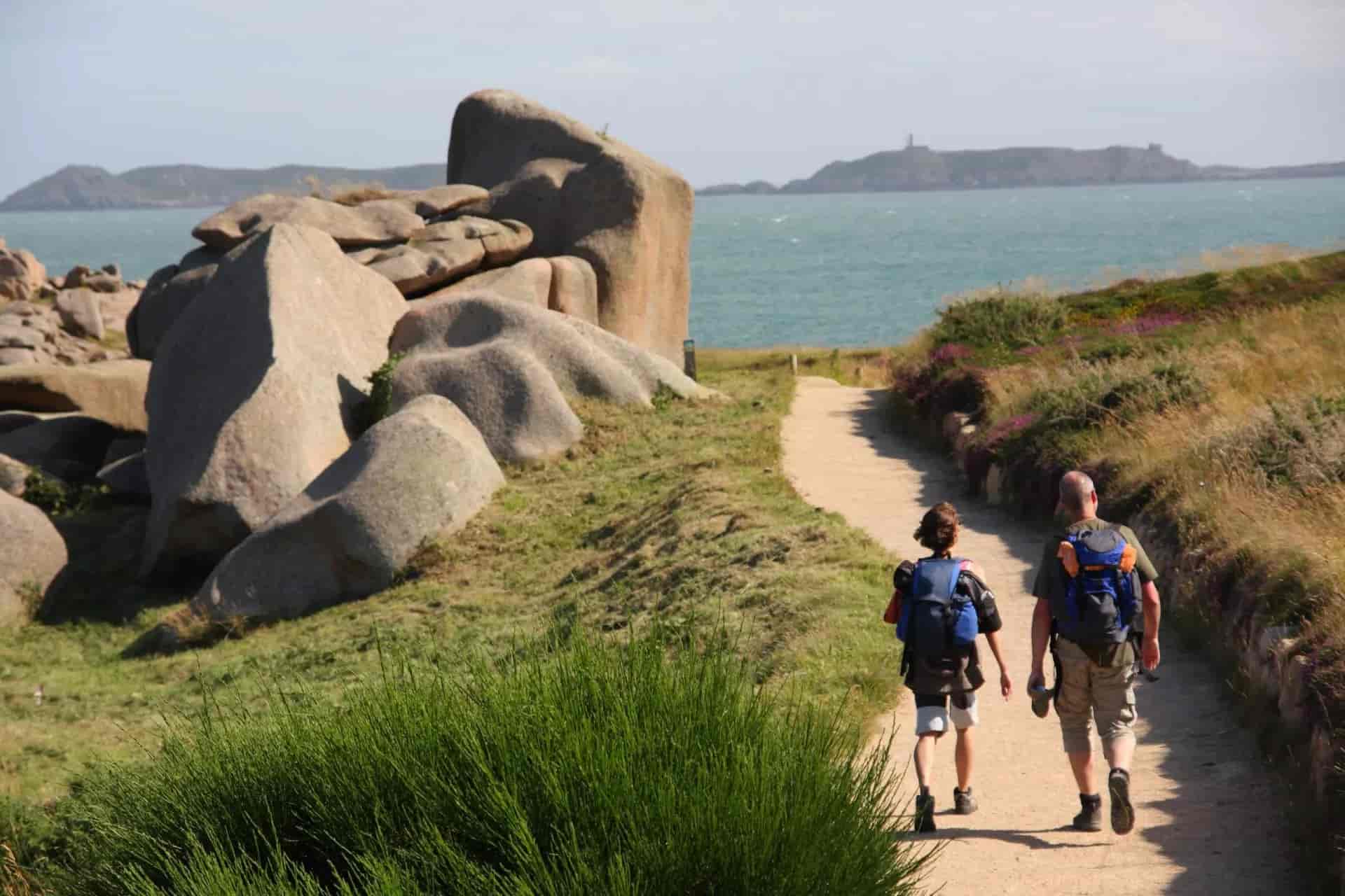 Hikers walking on path past pink granite boulders toward the sea, Pink Granite Coast