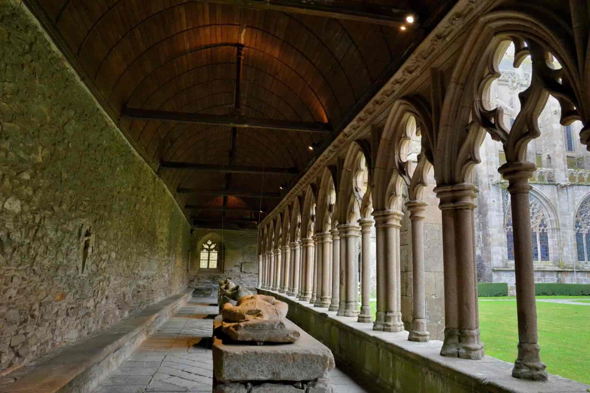 Cloister walkway with stone arches, wooden ceiling, and sarcophagi at the Tréguier Cathedral.
