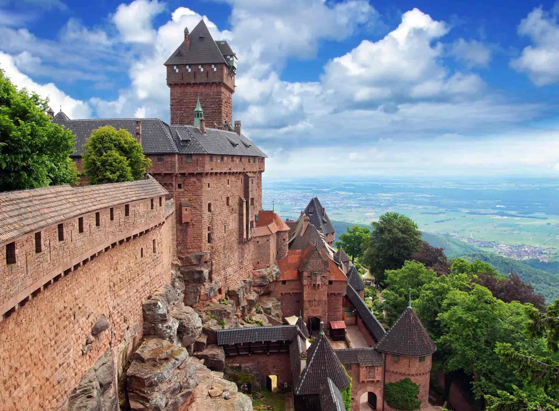 Château du Haut-Kœnigsbourg on a rocky outcrop overlooking a vast green valley under a blue sky.
