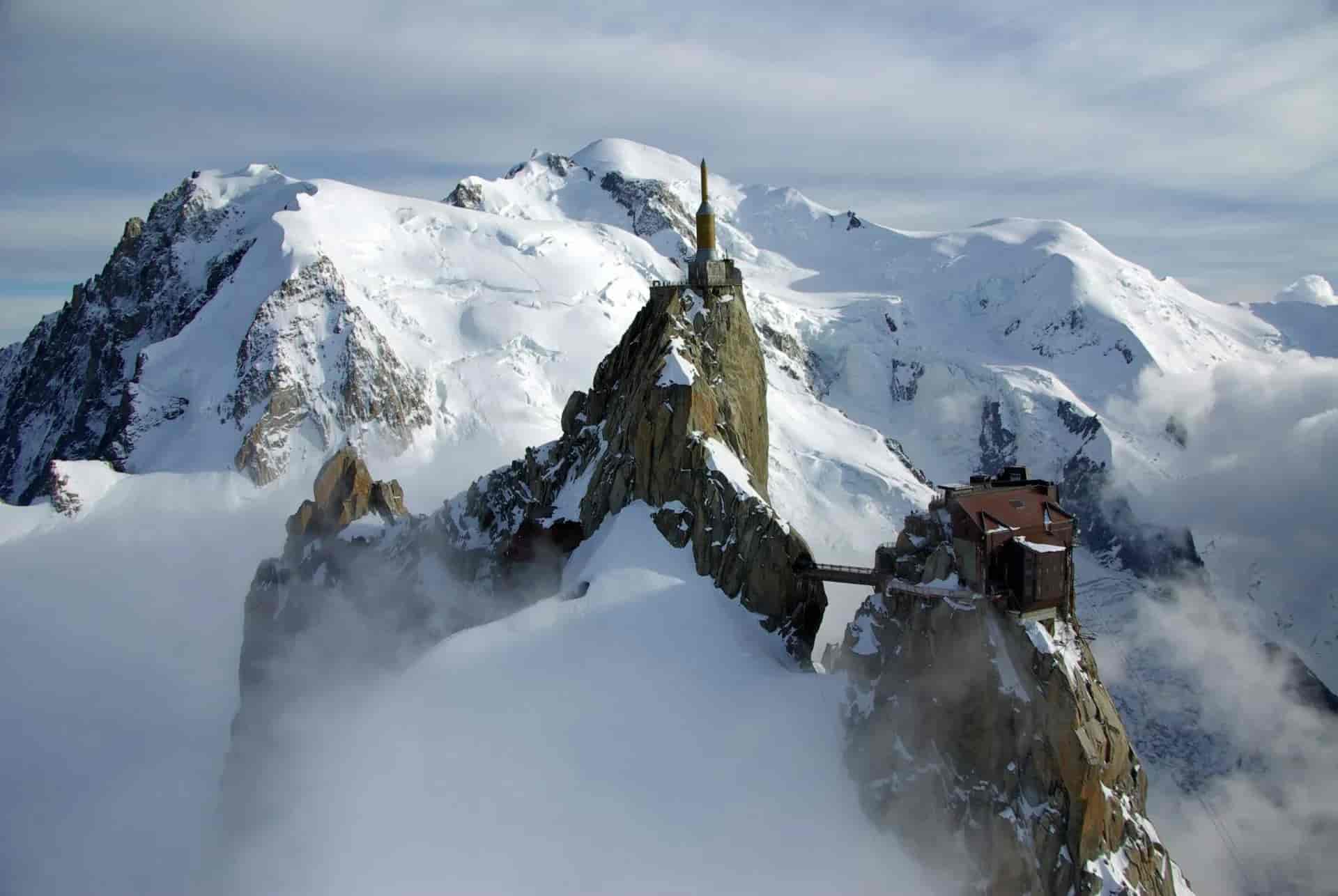 Aiguille du Midi station perched on a rocky spire amidst vast, snow-covered alpine mountains.