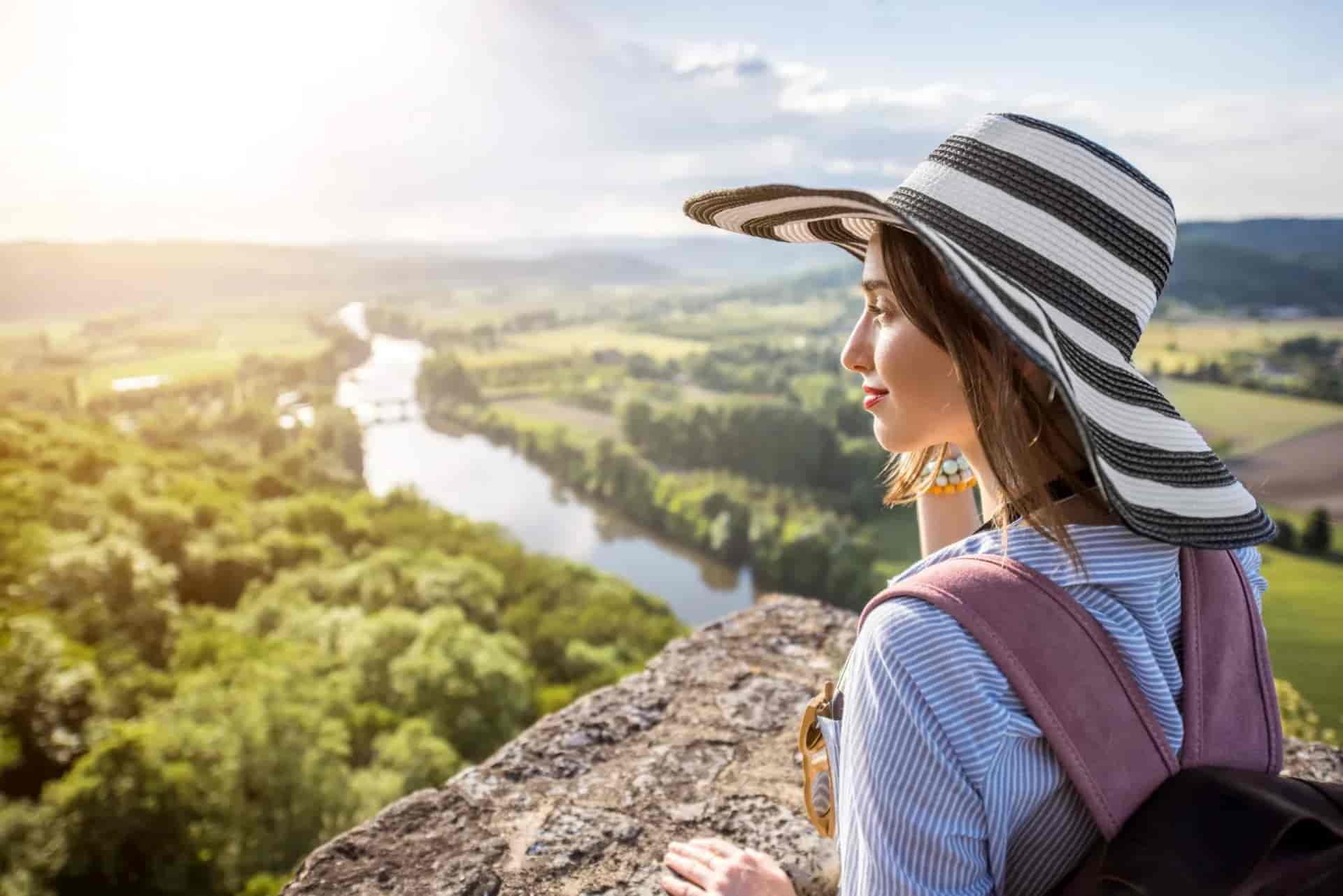 Hiker with striped hat overlooking lush green valley and winding river in Dordogne region.