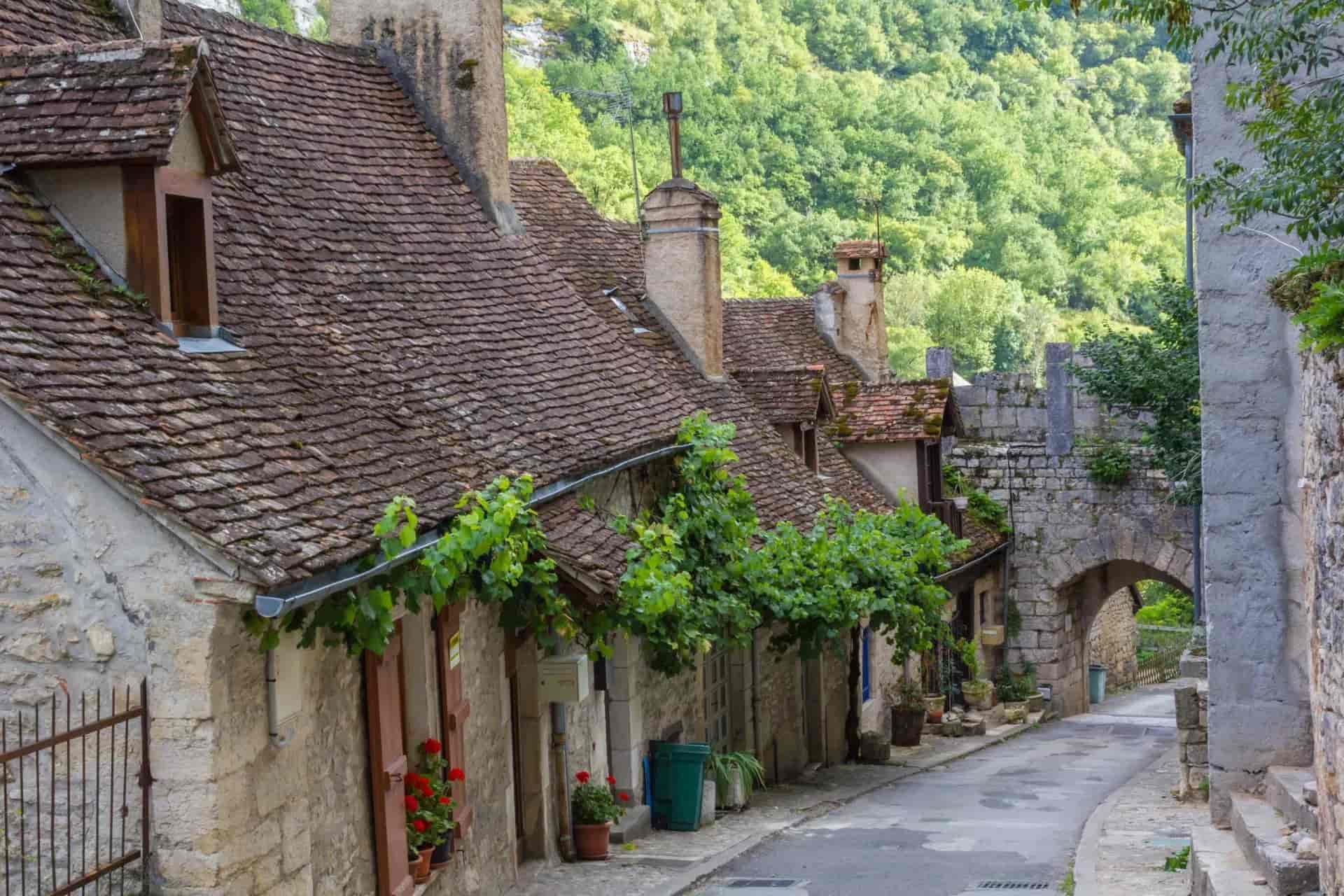 Stone buildings with tiled roofs line a narrow street leading to an arched stone gateway in Rocamadour.