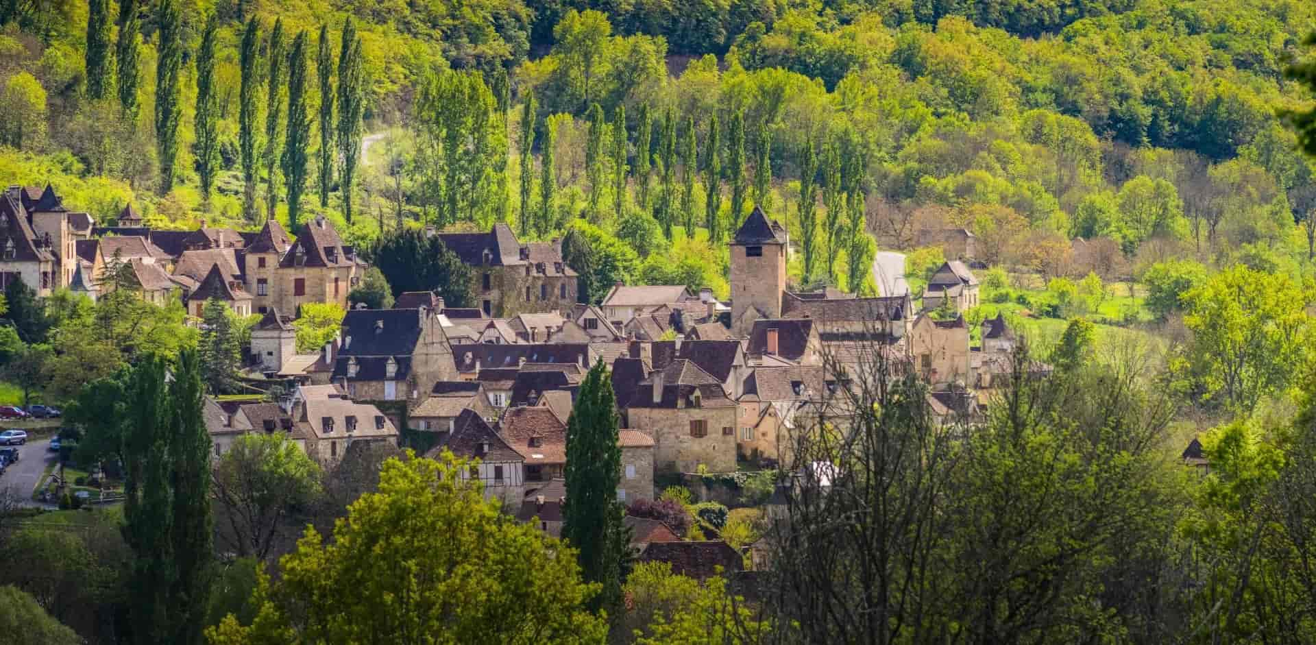 Historic European village nestled in lush green hillsides with stone buildings and terracotta roofs.