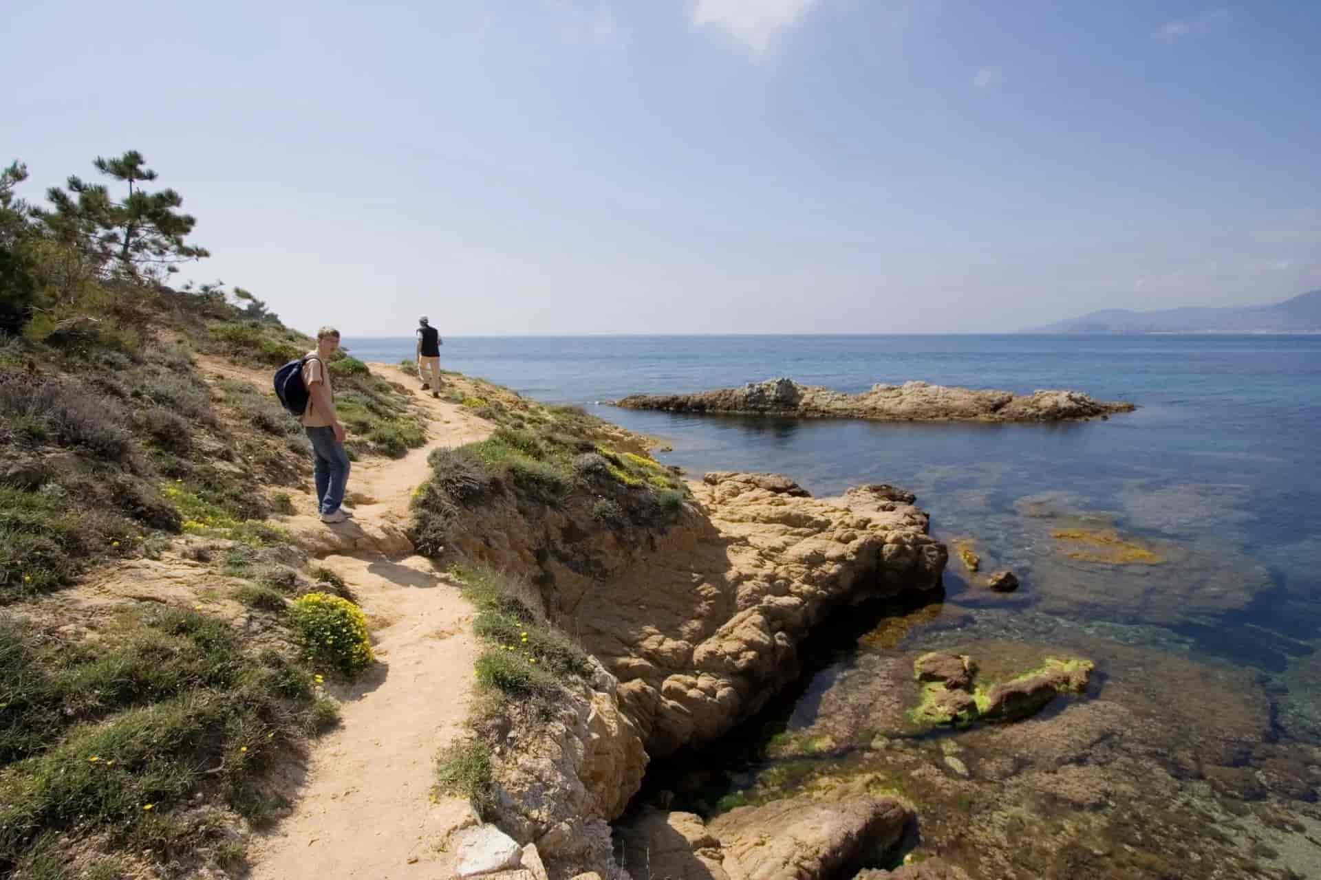 Hikers on coastal path above clear blue sea with rocky shoreline, French Riviera