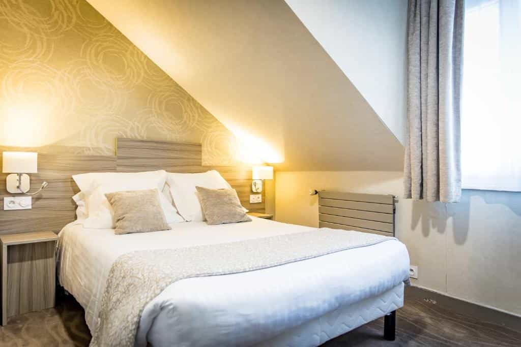 Hotel room with white bedding under an angled ceiling, illuminated by bedside lamps.