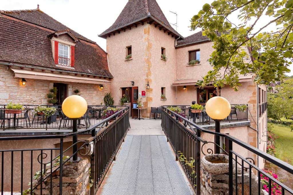 Stone building with outdoor dining terraces connected by a metal walkway in Loubressac.