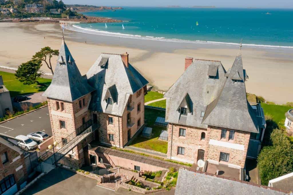 Stone buildings with steep slate roofs near a sandy beach and turquoise sea in Ploumanac'h.