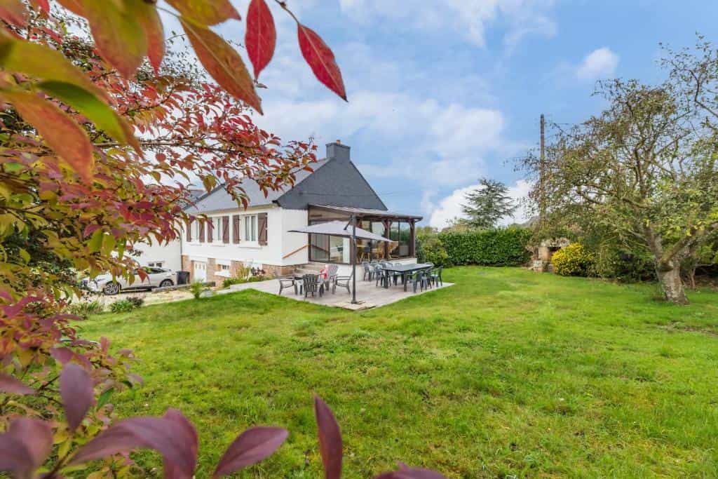 White house with dark roof, patio dining area, and large grassy yard framed by autumn leaves.
