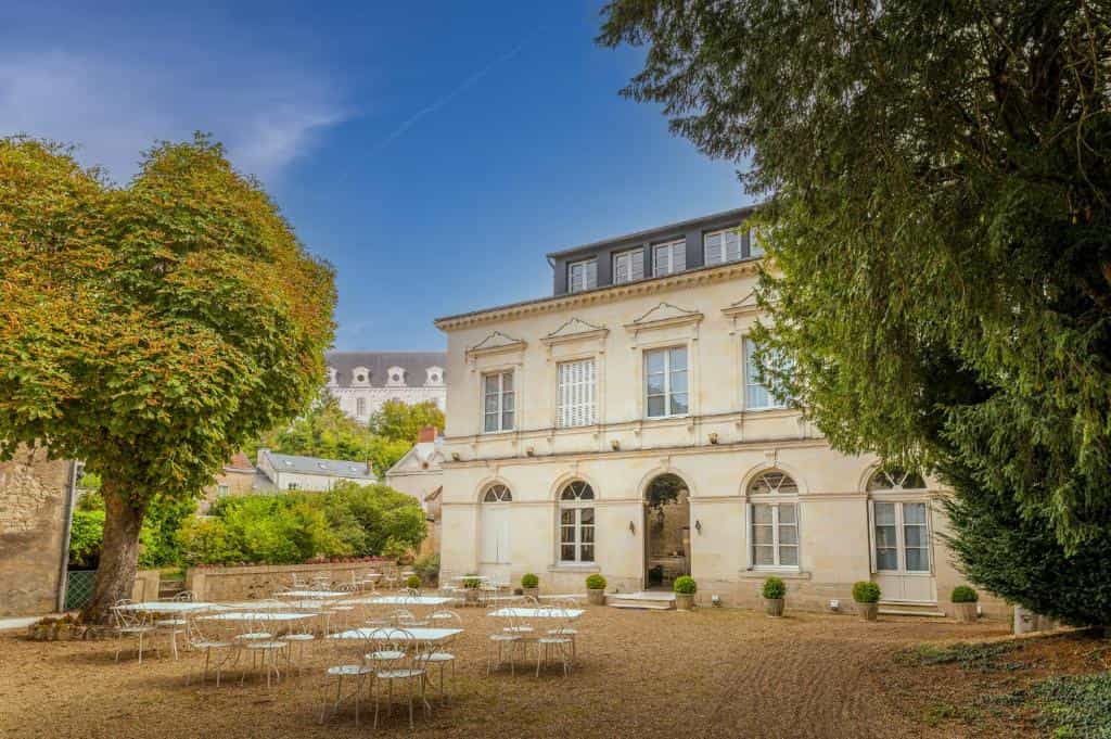 Hôtel Le Grand Monarque exterior with outdoor seating area and large trees under blue sky