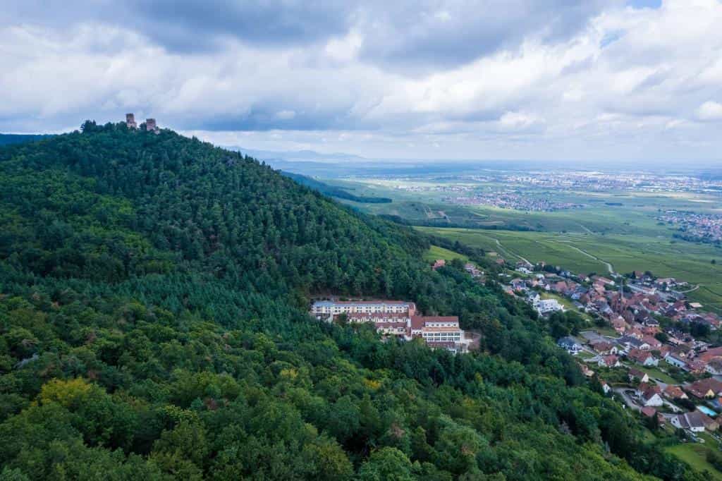 Hotel and spa building nestled in a dense forest overlooking a village and valley in Husseren.