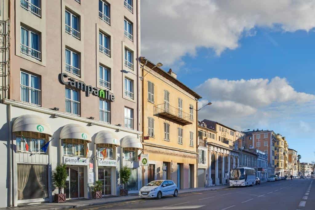 Campanile hotel exterior on a street with parked cars and a bus under a blue sky.