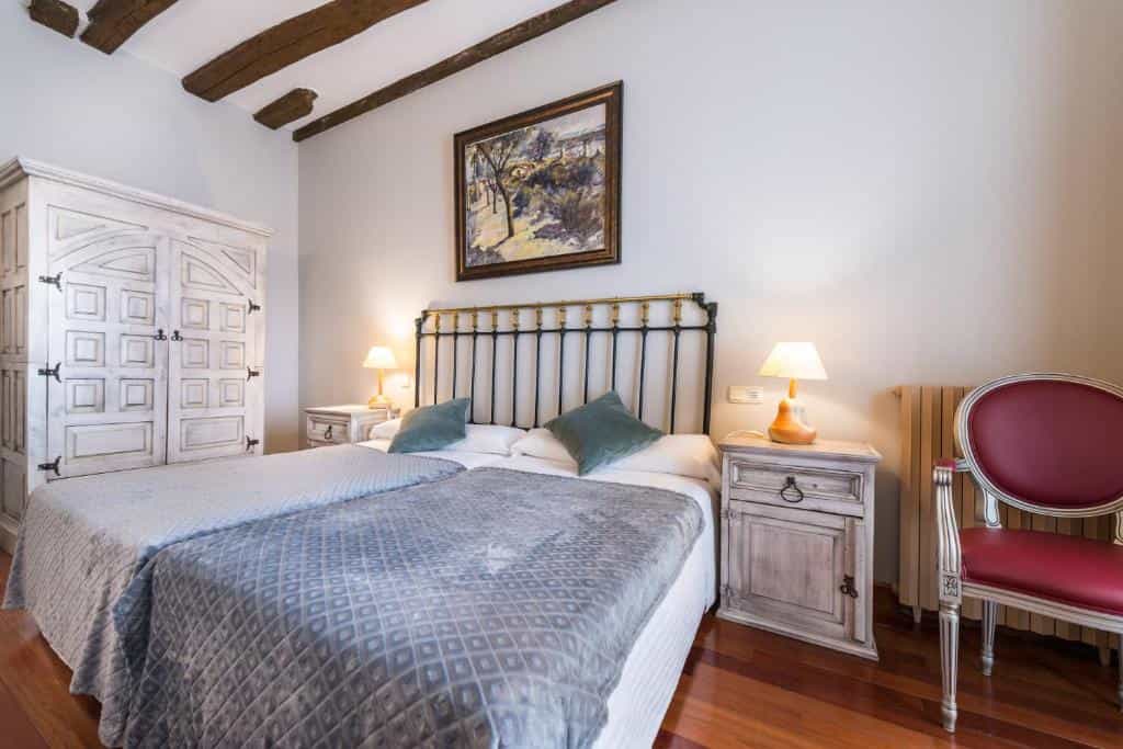 Twin beds with metal headboard, white distressed wardrobe, and exposed wood beams in Hotel Alda Vía León.