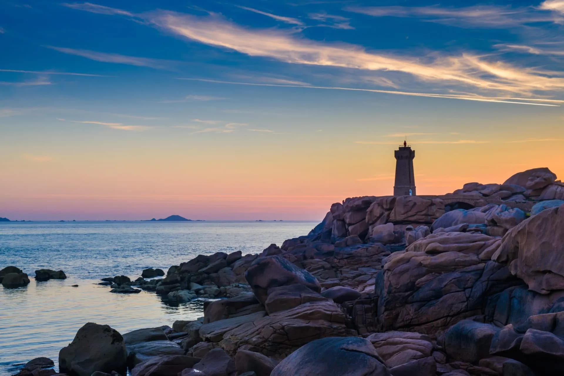 Lighthouse on rocky coast at sunset in Ploumanac'h with colorful sky over the sea.