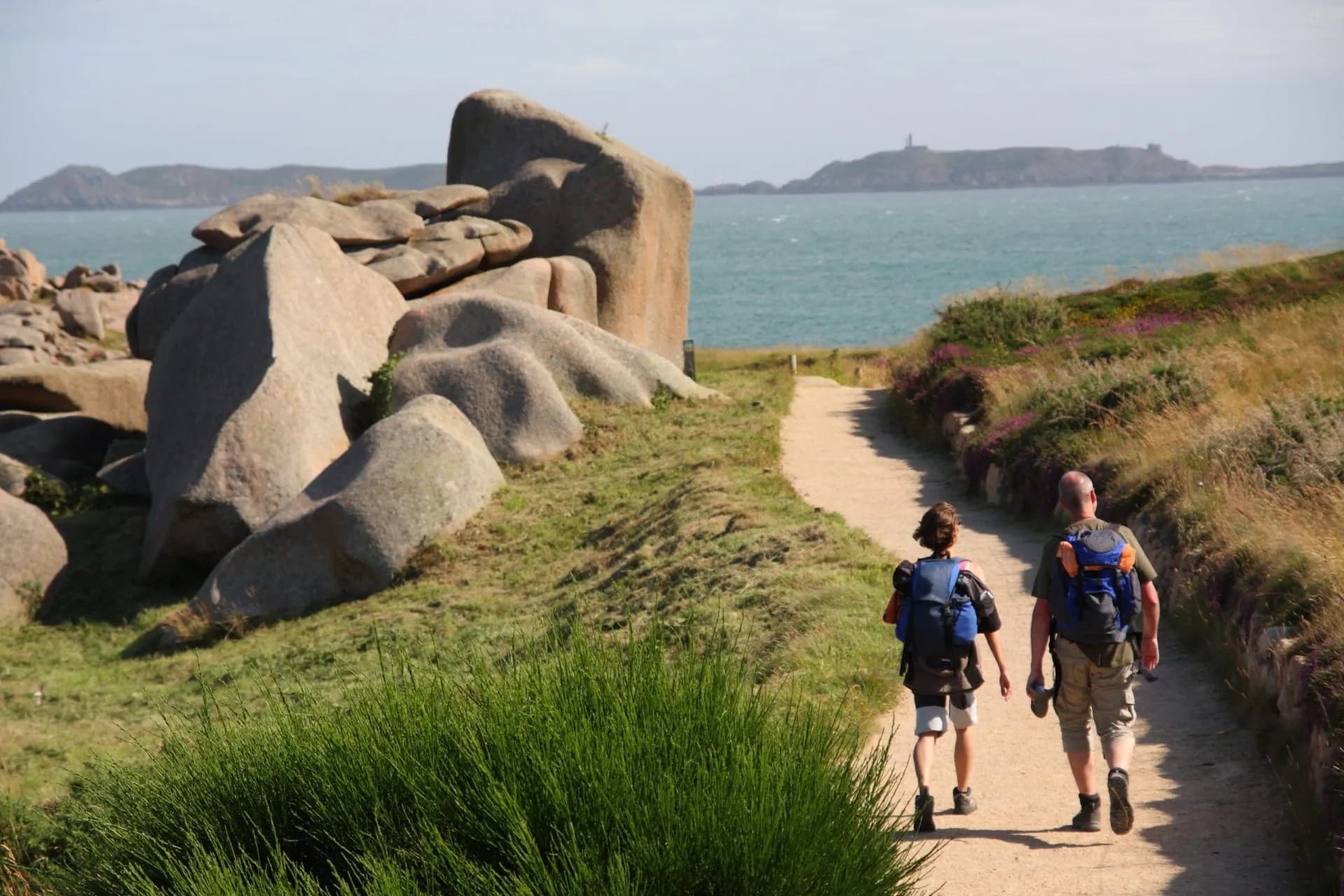 Hikers walking on path past pink granite boulders toward the sea, Pink Granite Coast