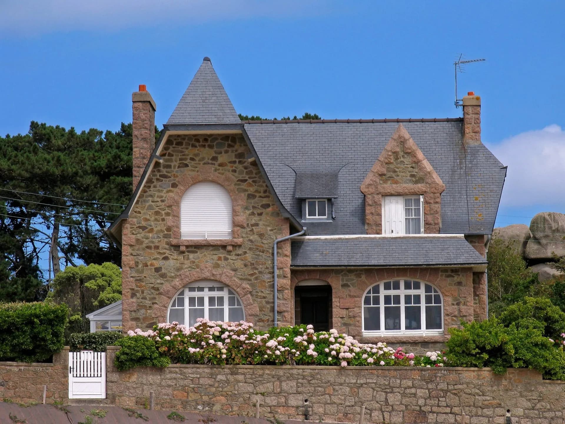 Stone house in Ploumanac'h with slate roof, pink hydrangeas, and stone wall