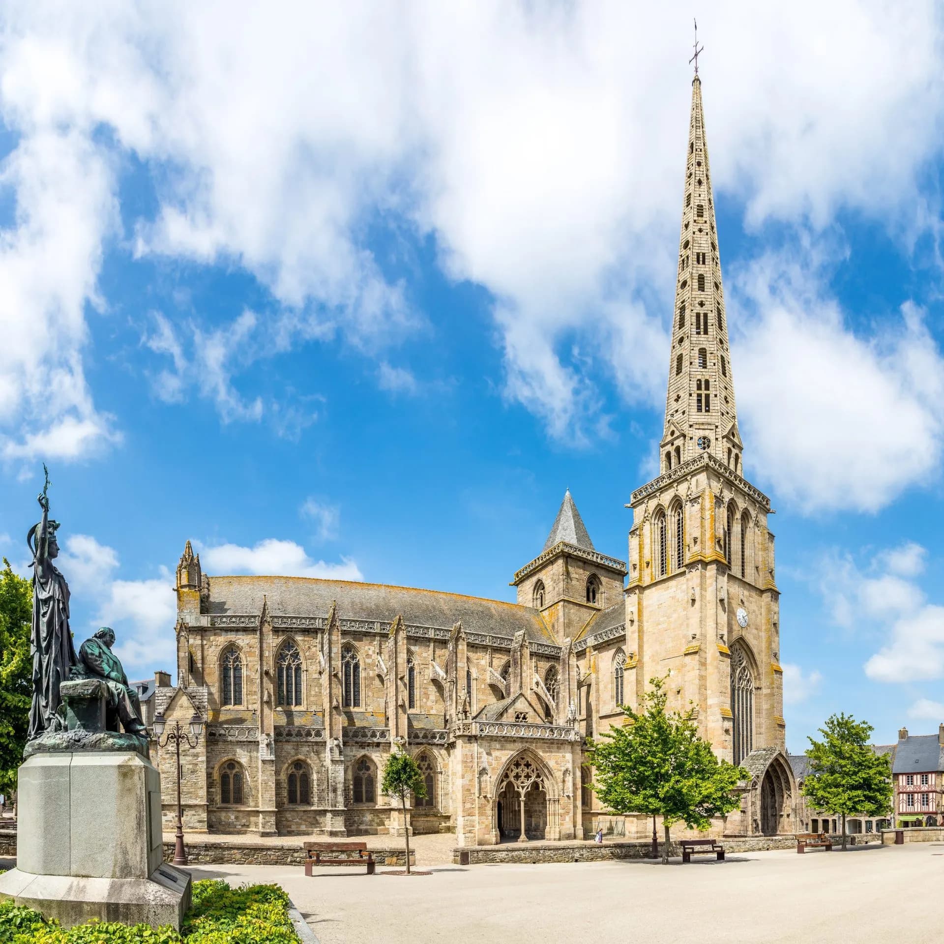 Cathedral of Saint-Tugdual with tall stone spire and statue in sunny town square.