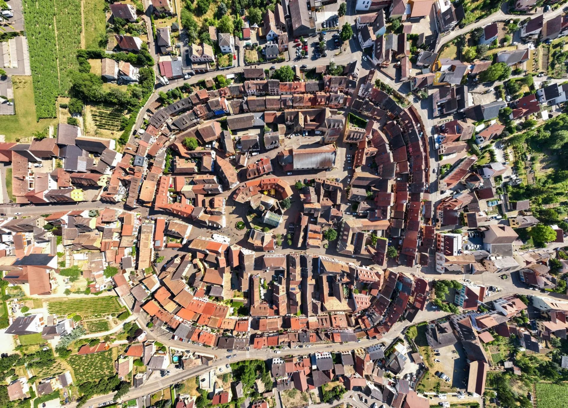 Bird's-eye view of Eguisheim's circular medieval town center with red roofs and surrounding vineyards.