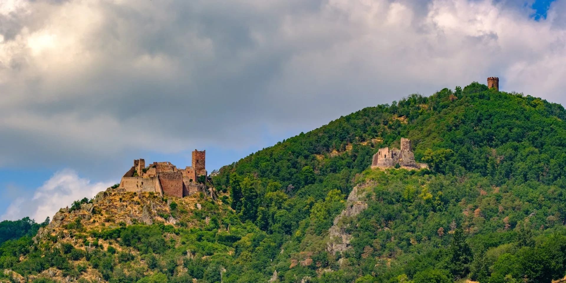 Ruins of three chateaux above a densely forested hill under a cloudy sky near Eguisheim.