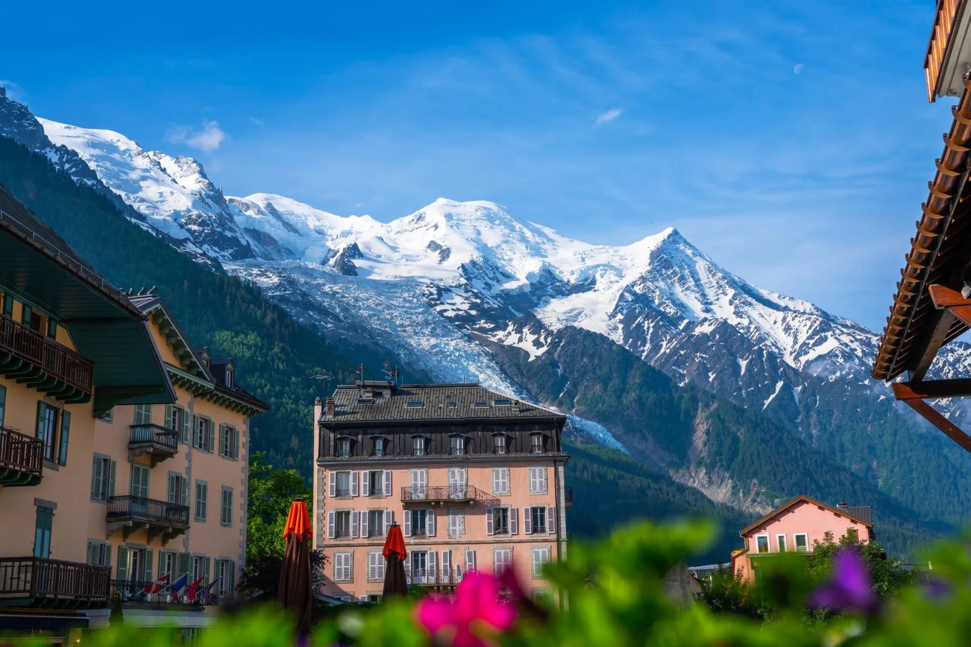 Chamonix town center buildings with snow-capped mountains and glacier under a bright blue sky.