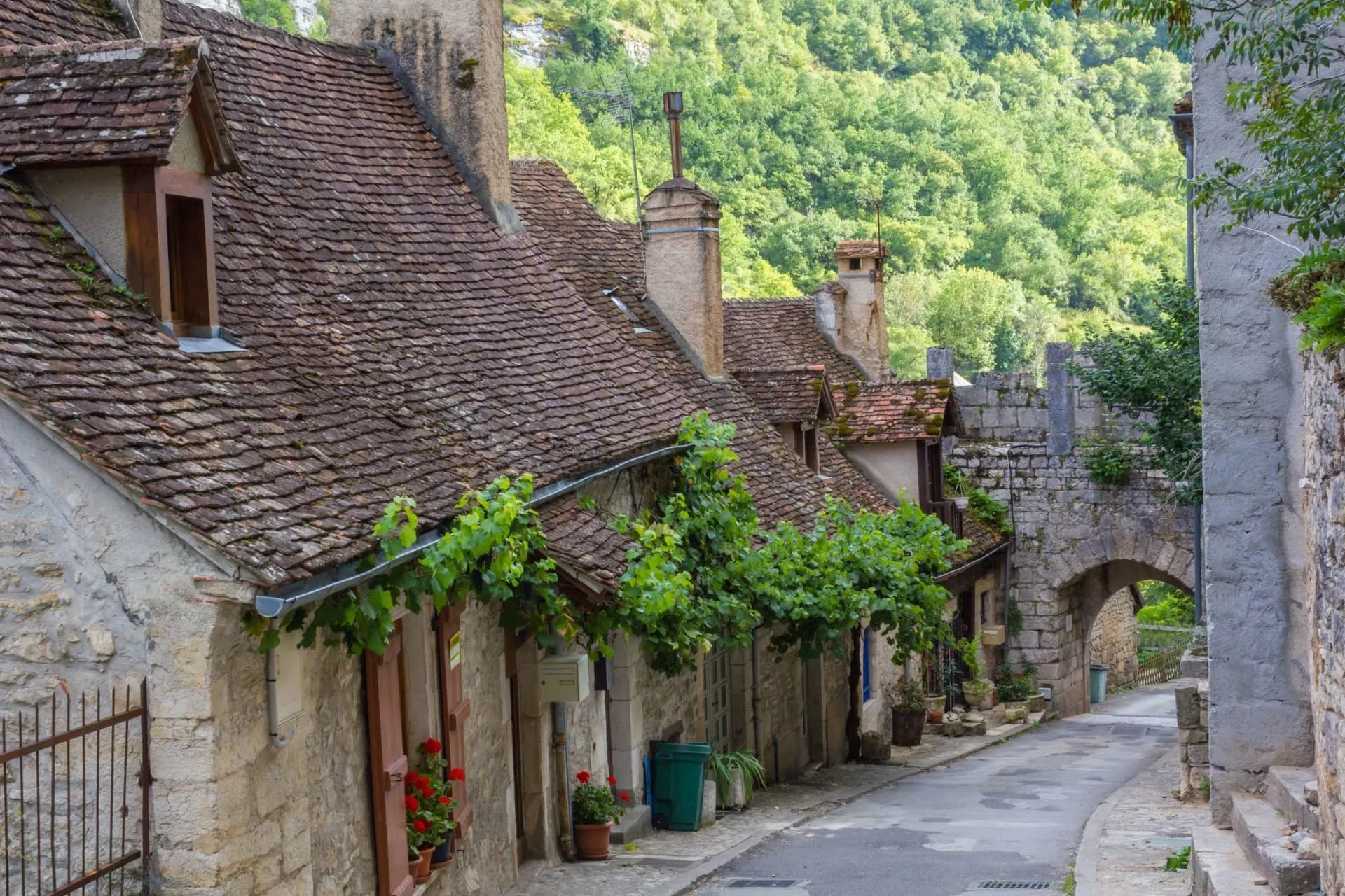 Stone buildings with tiled roofs line a narrow street leading to an arched stone gateway in Rocamadour.