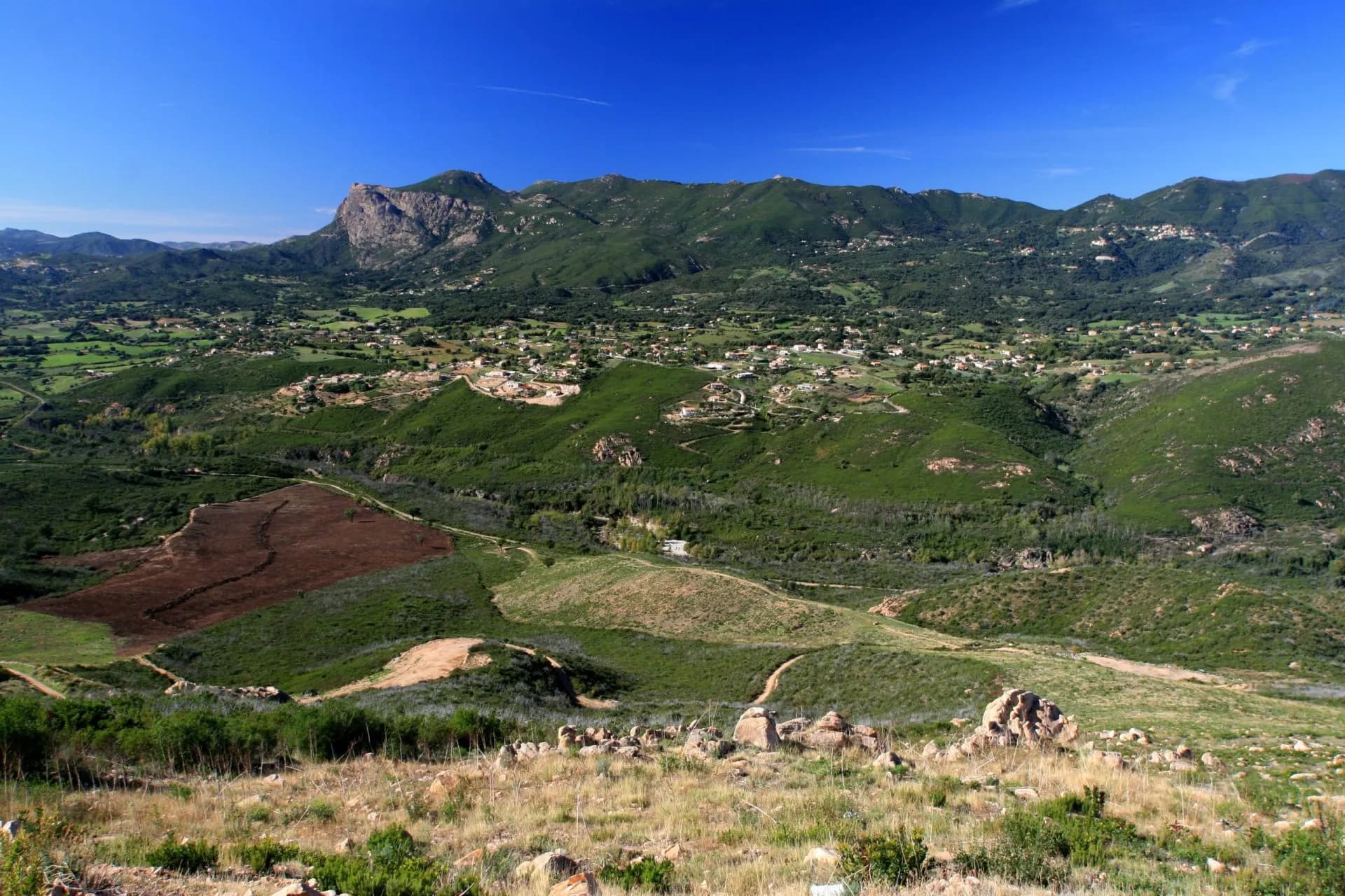 Green hills and mountains with scattered villages under a clear blue sky in Corsica.