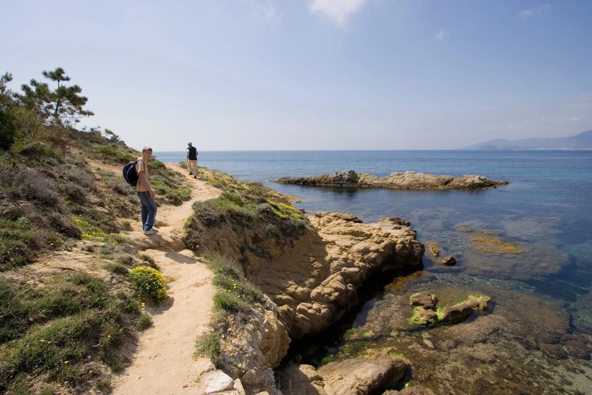 Hikers on coastal path above clear blue sea with rocky shoreline, French Riviera