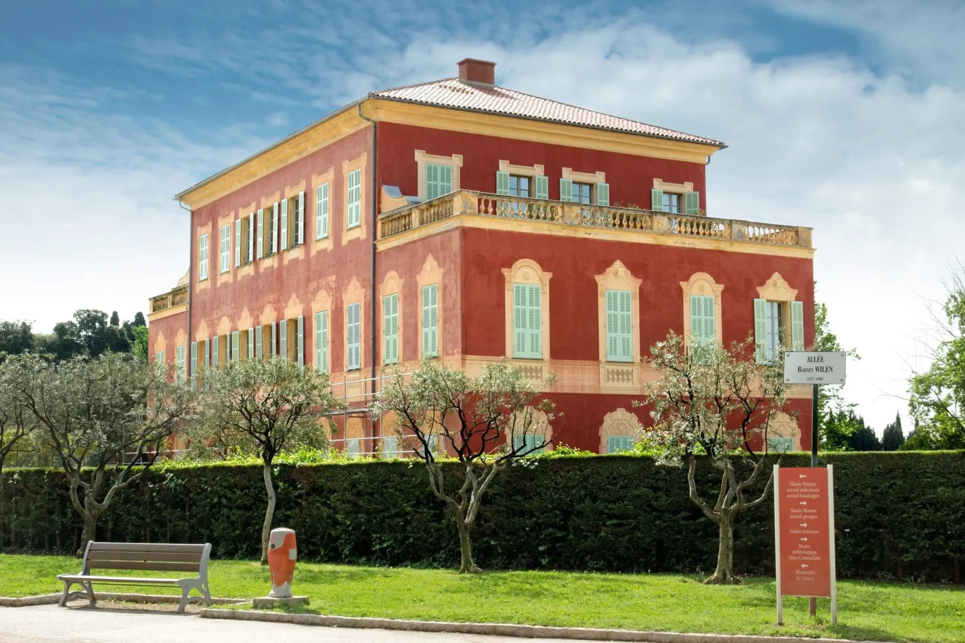 Red building with light green shutters, likely the Matisse Museum, viewed from a grassy area.