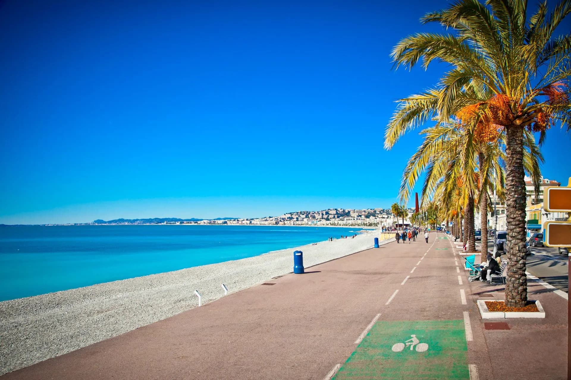Promenade des Anglais in Nice with palm trees, turquoise sea, and city skyline.