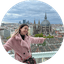 Woman in pink coat overlooking city skyline with historic church dome.