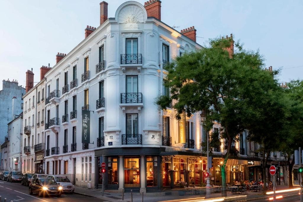 Hotel Saint Regis building facade at dusk on a city street with traffic and trees.