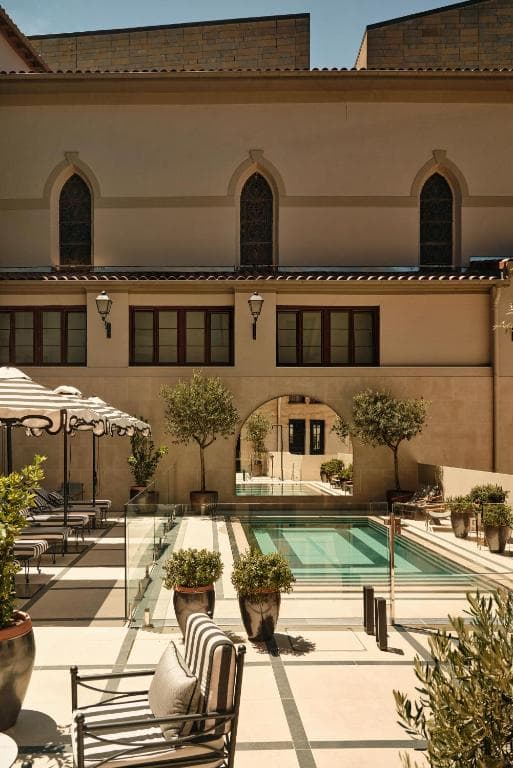 Courtyard pool area with striped umbrellas, potted trees, and arched architectural details.