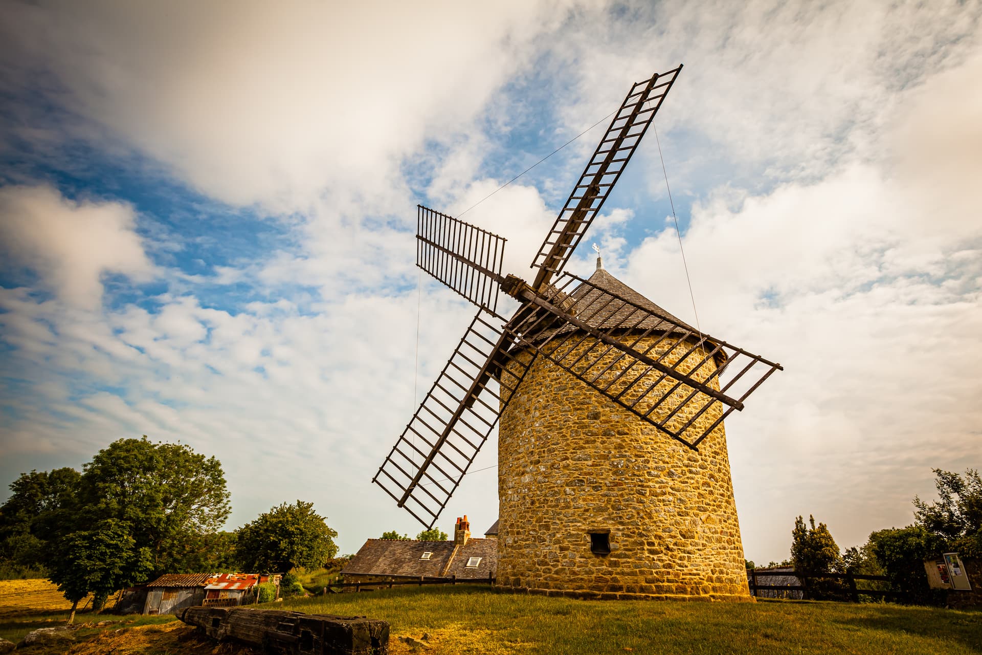 Stone windmill with large wooden sails in a grassy field near Dol-de-Bretagne, France.