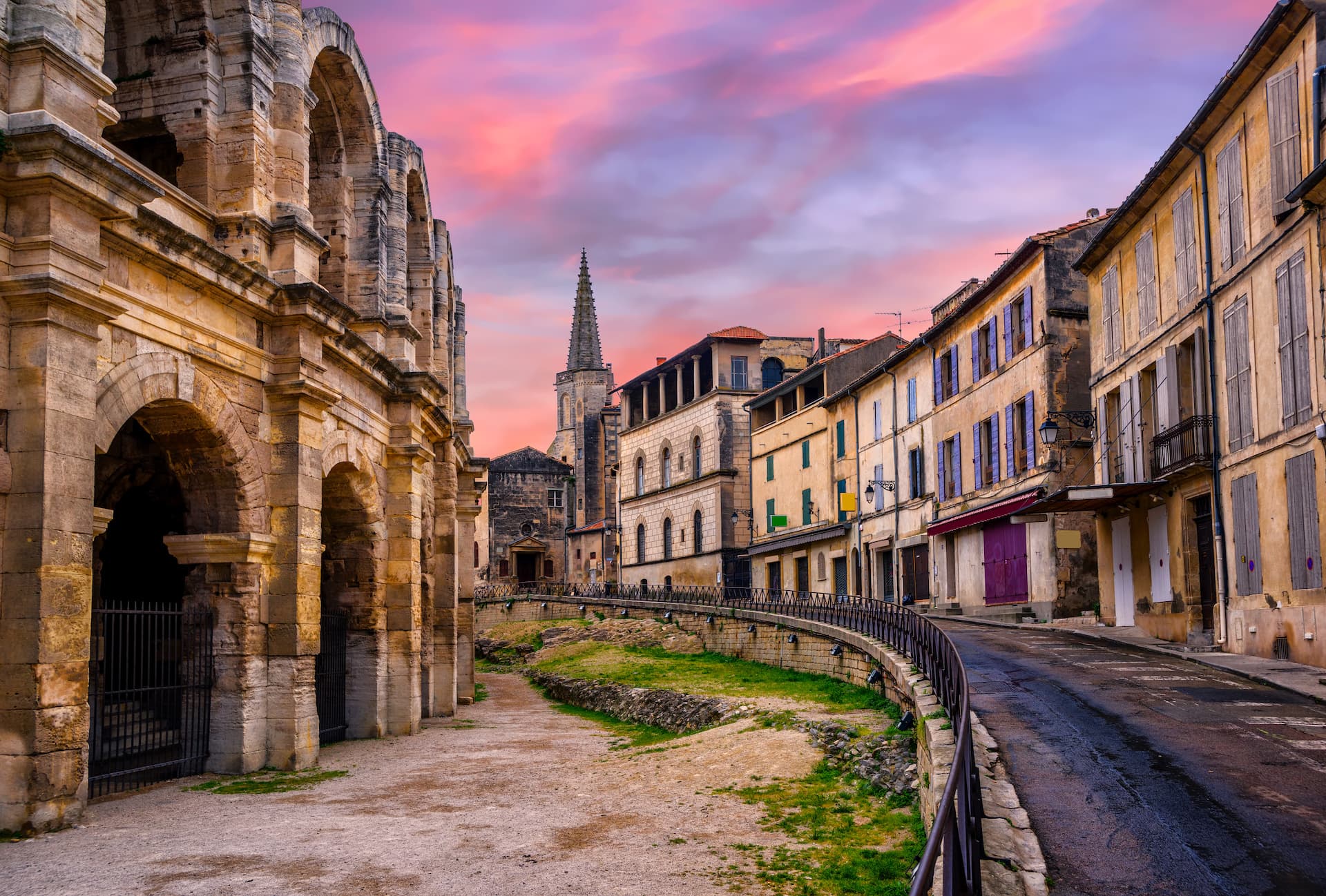 Arles Roman Amphitheatre exterior beside curved street at sunset with pink sky