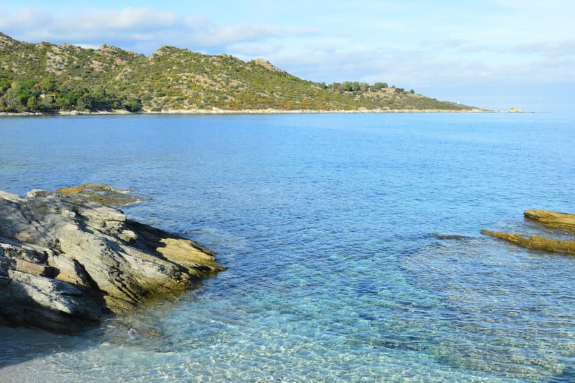 Clear blue coastal waters with rocky shore and green hills