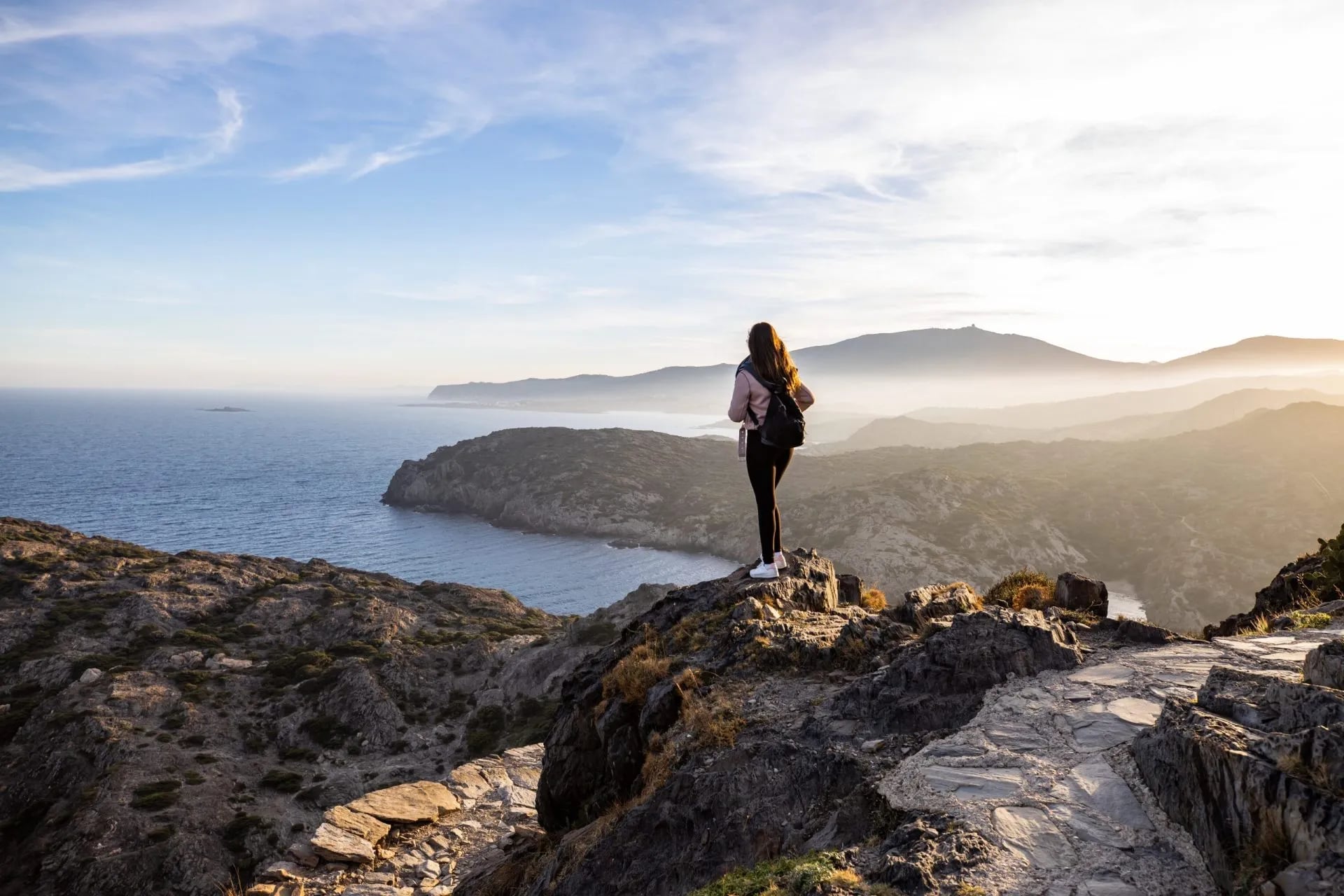 Hiker overlooking Cap de Creus rugged coastline and hazy mountains at sunset