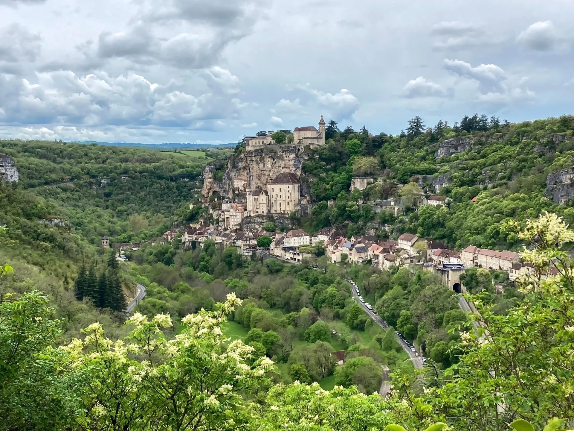 Rocamadour village built into a cliffside overlooking a lush green valley under cloudy skies.