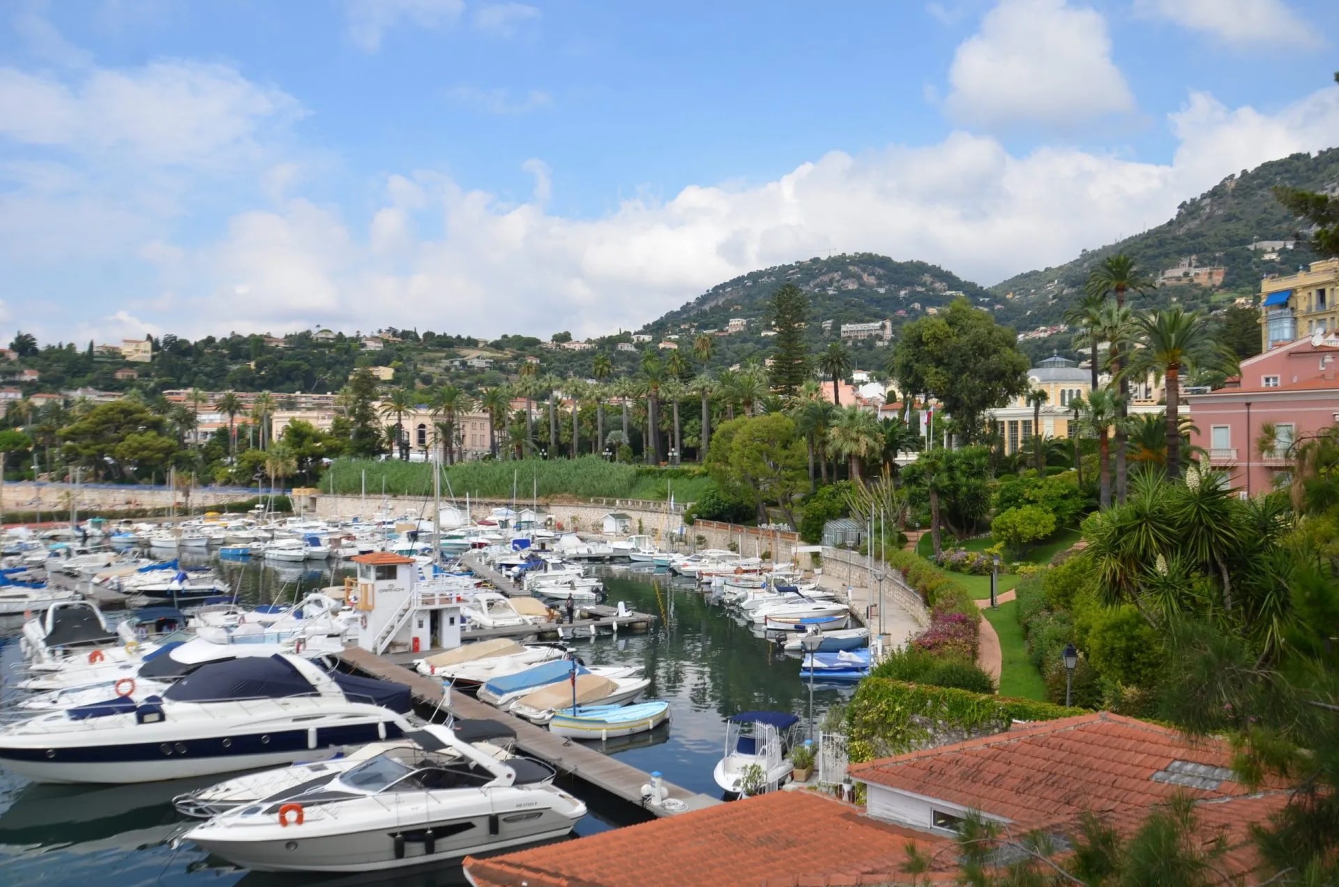 Yachts and boats docked in a harbor with lush green hills and buildings in Beaulieu-sur-Mer.