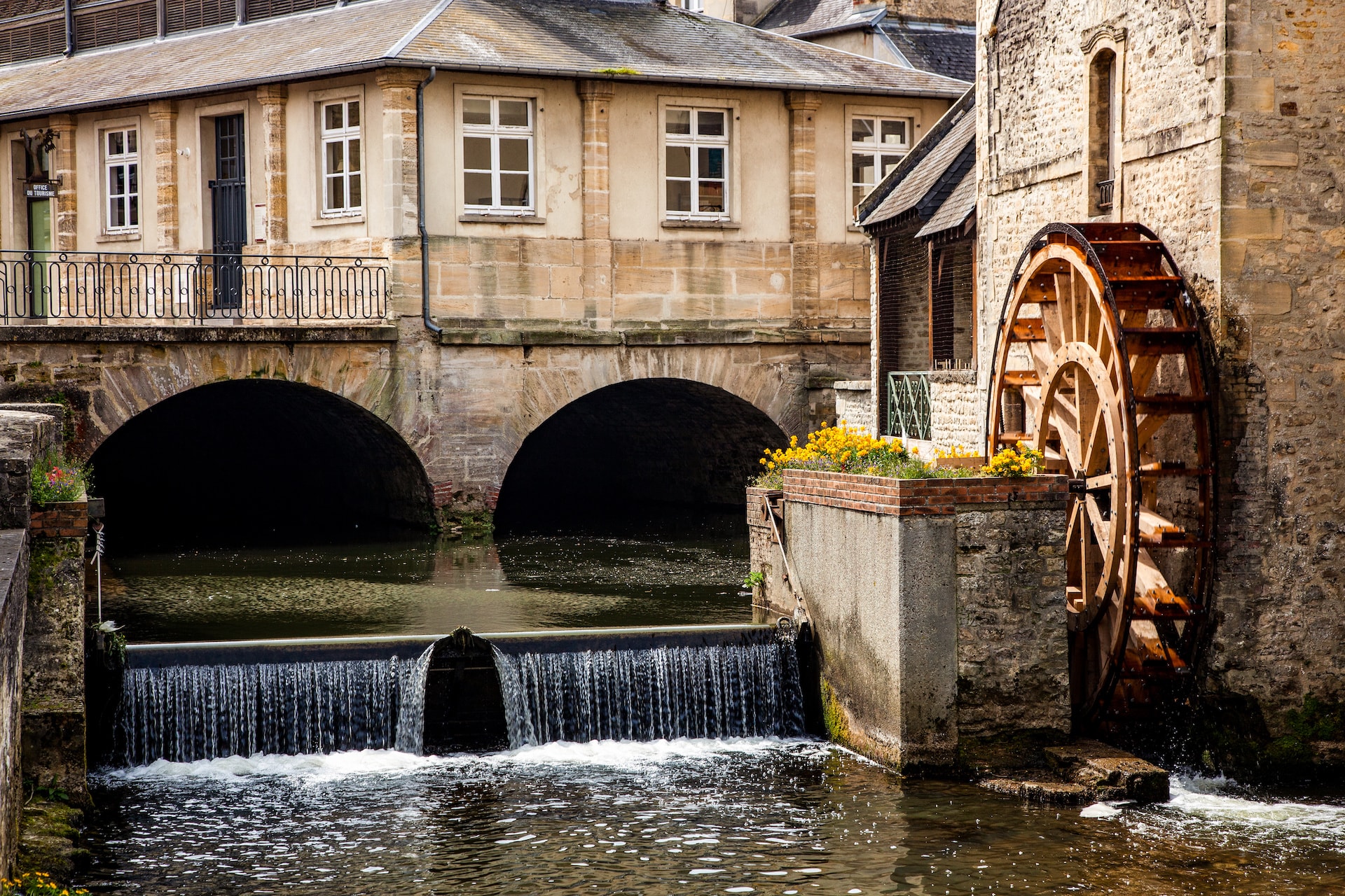 Historic watermill with large wooden wheel next to stone building and small waterfall.