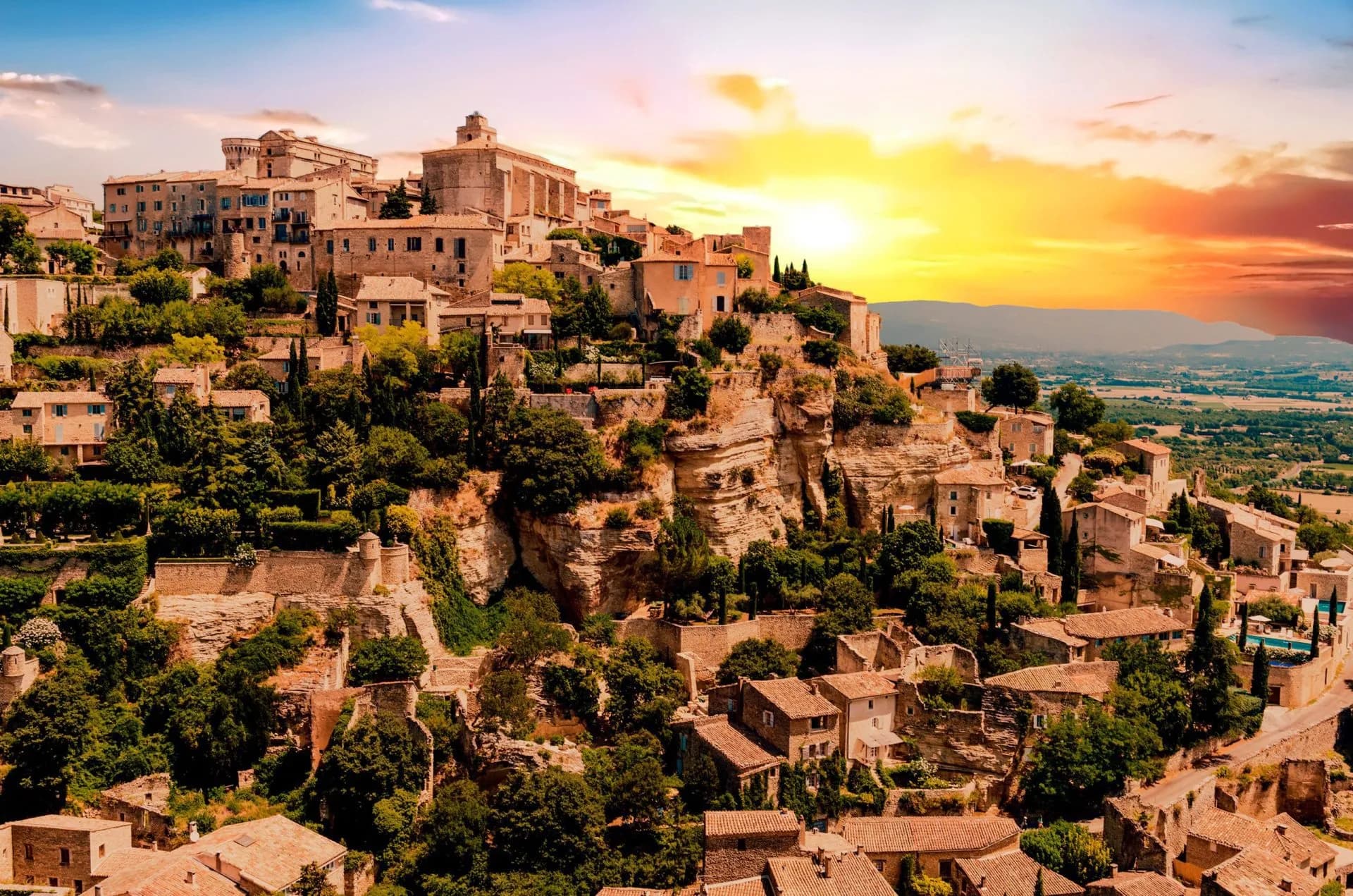 Hilltop village with stone buildings nestled into cliffs at sunset, Gordes, France