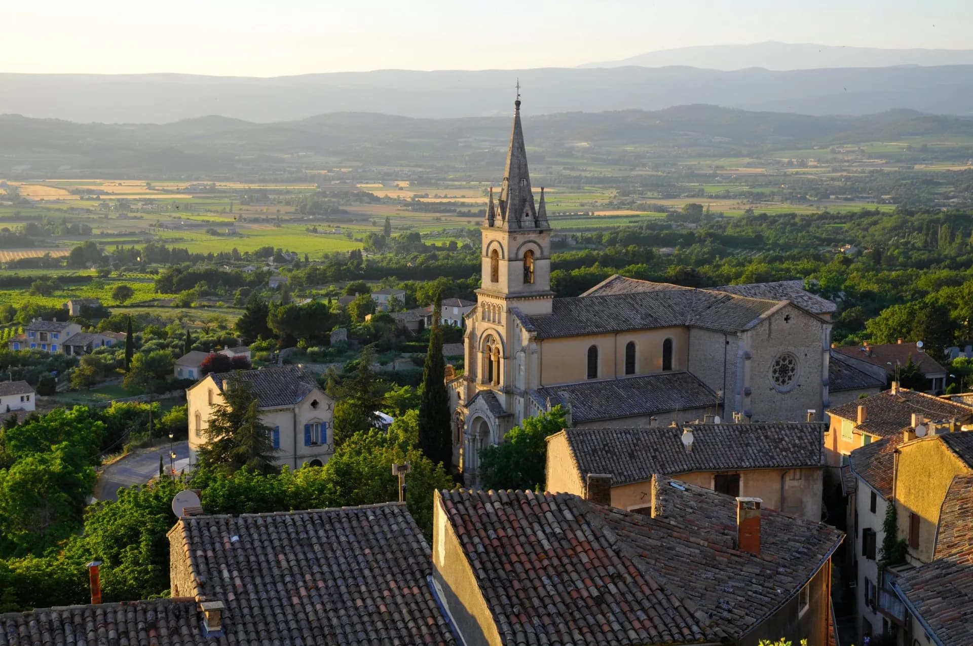 Church spire overlooking tiled roofs and green valley near Bonnieux in the Luberon mountains.