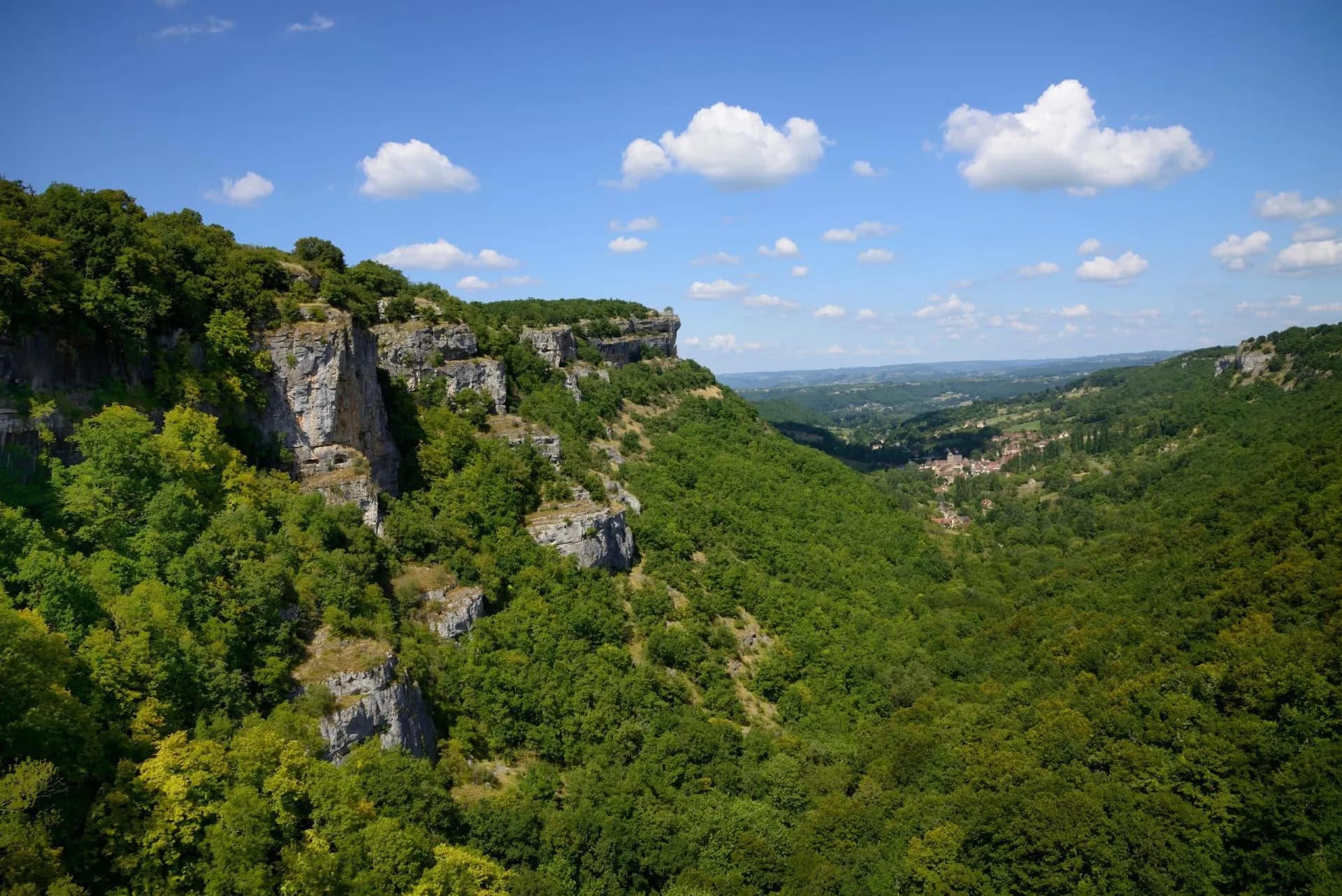 Lush green valley with steep forested cliffs under a blue sky with white clouds.