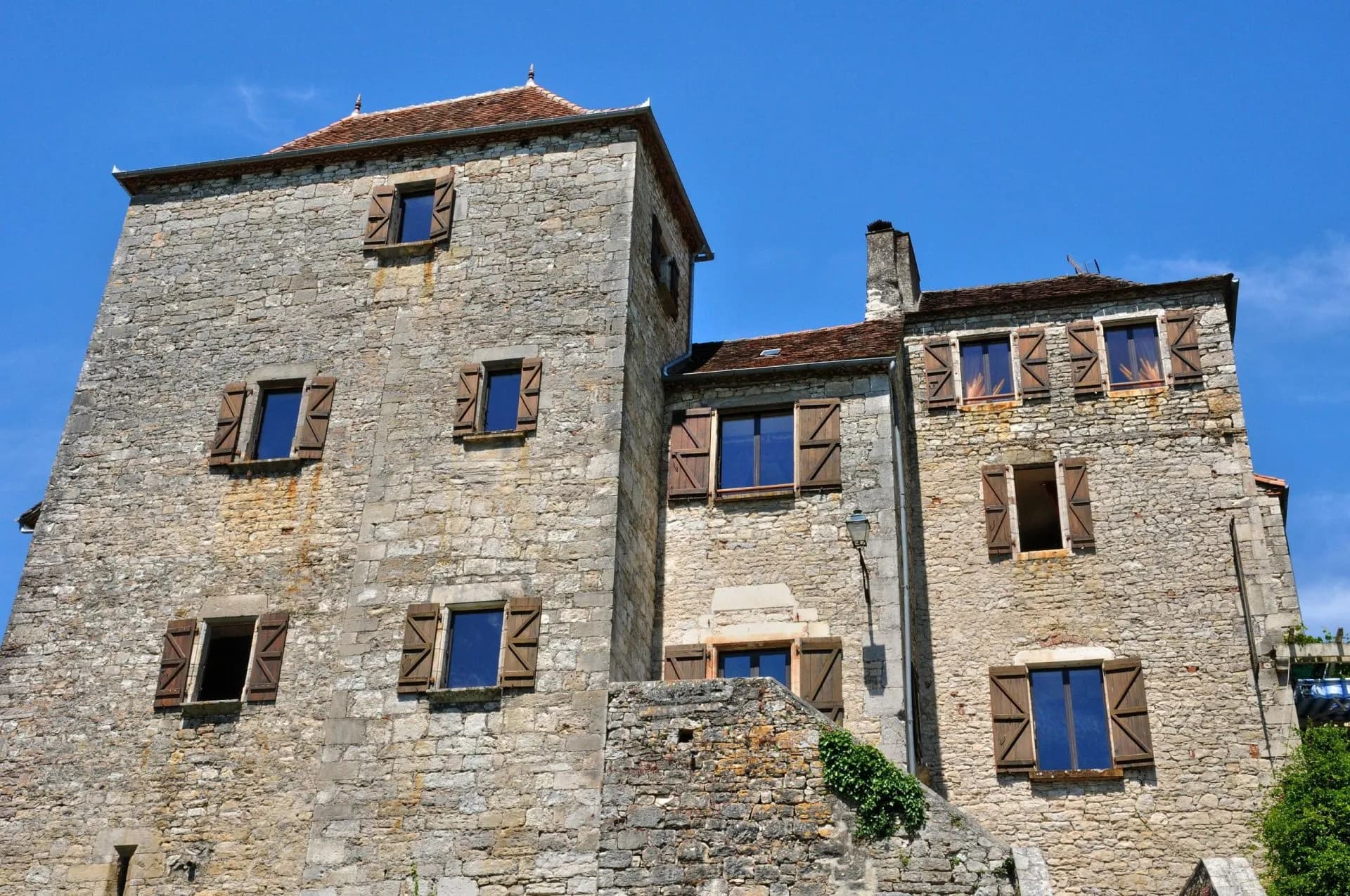 Old stone buildings with wooden shutters against a clear blue sky in Meyronne.