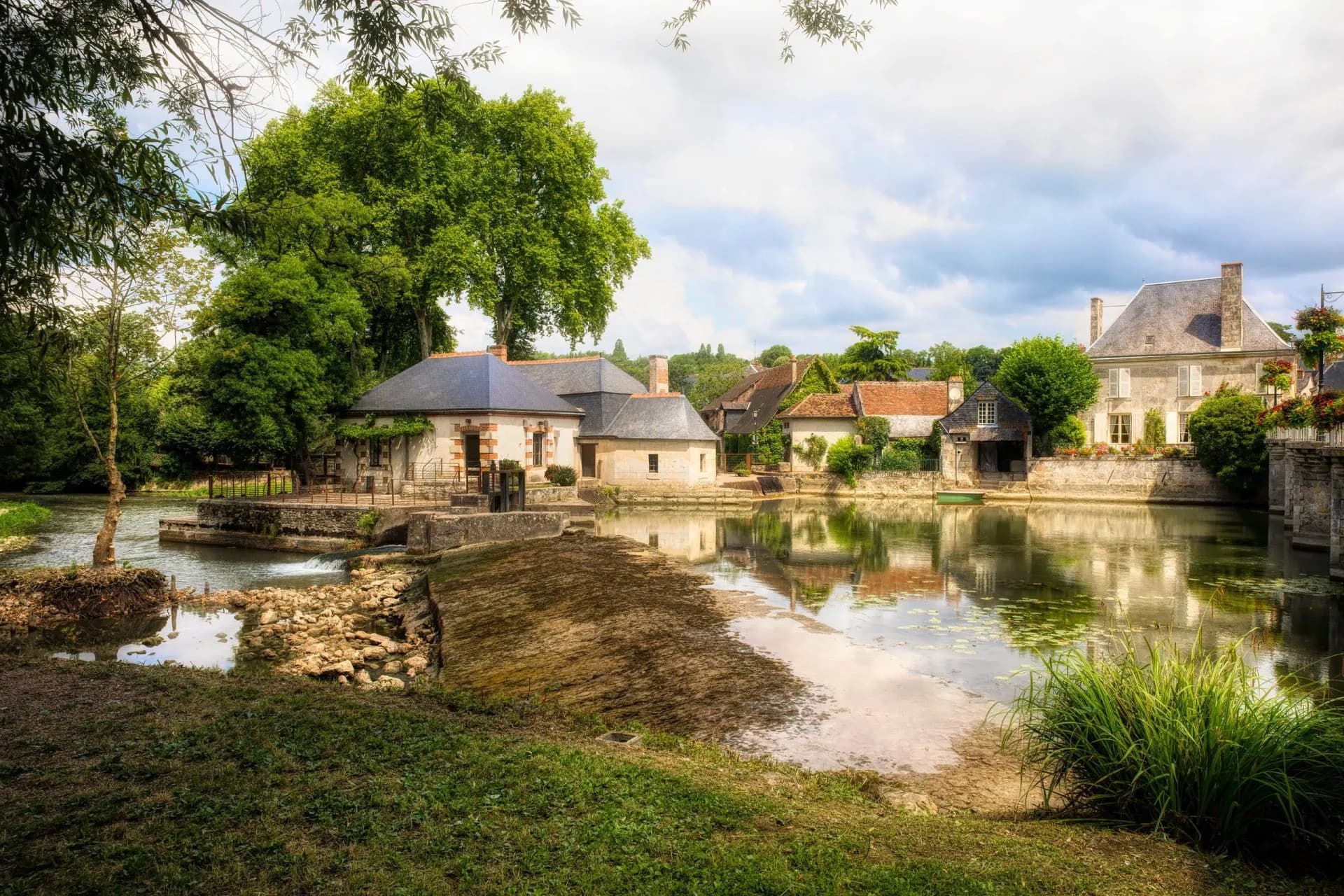 Old water mill on the Indre River with stone houses reflecting in the calm water.