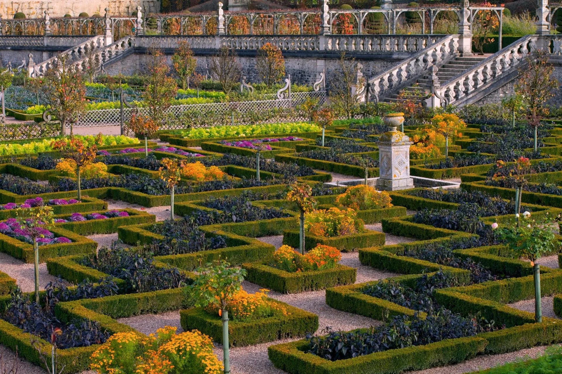 Formal gardens with geometric hedges, colorful autumn plantings, and a grand stone staircase.