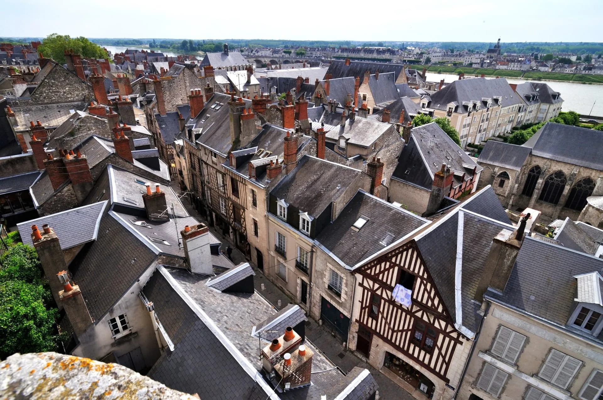 Rooftops with slate tiles and brick chimneys overlooking a narrow street in Amboise with a river in the distance.