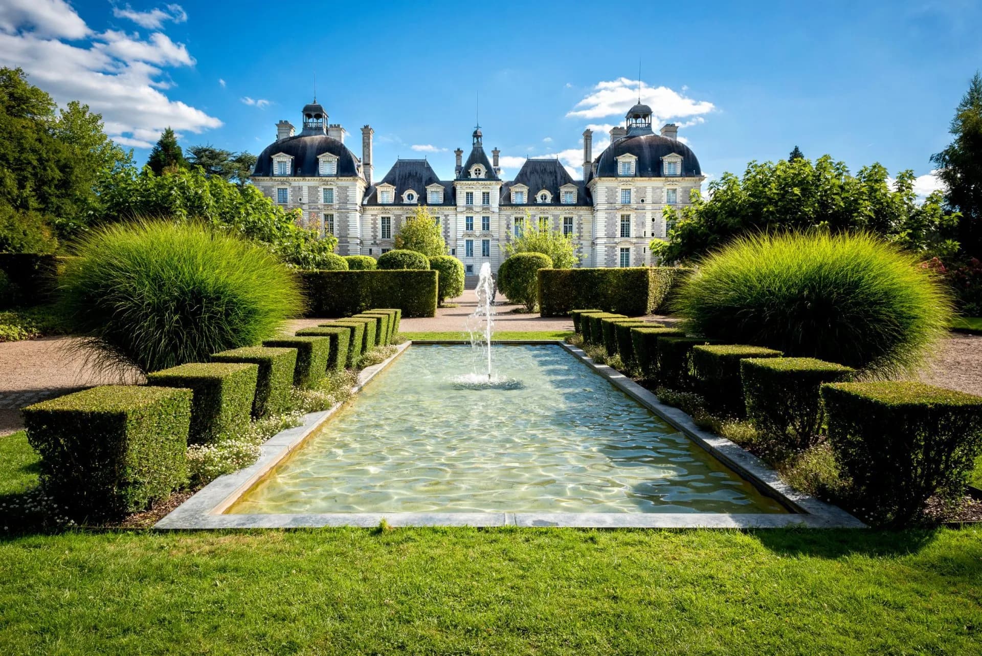 Chateau de Cheverny gardens with fountain, manicured hedges, and grand architecture under blue sky.
