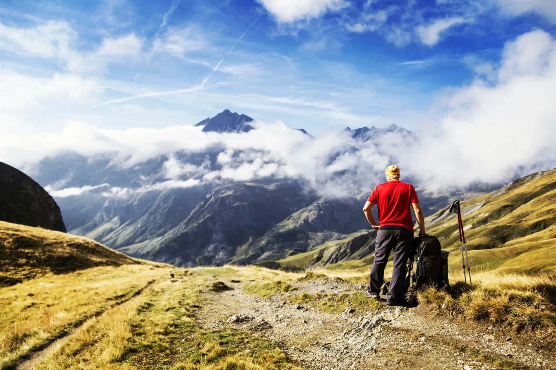 Hiker with backpack and poles overlooking Tour du Mont Blanc mountains partially covered by clouds