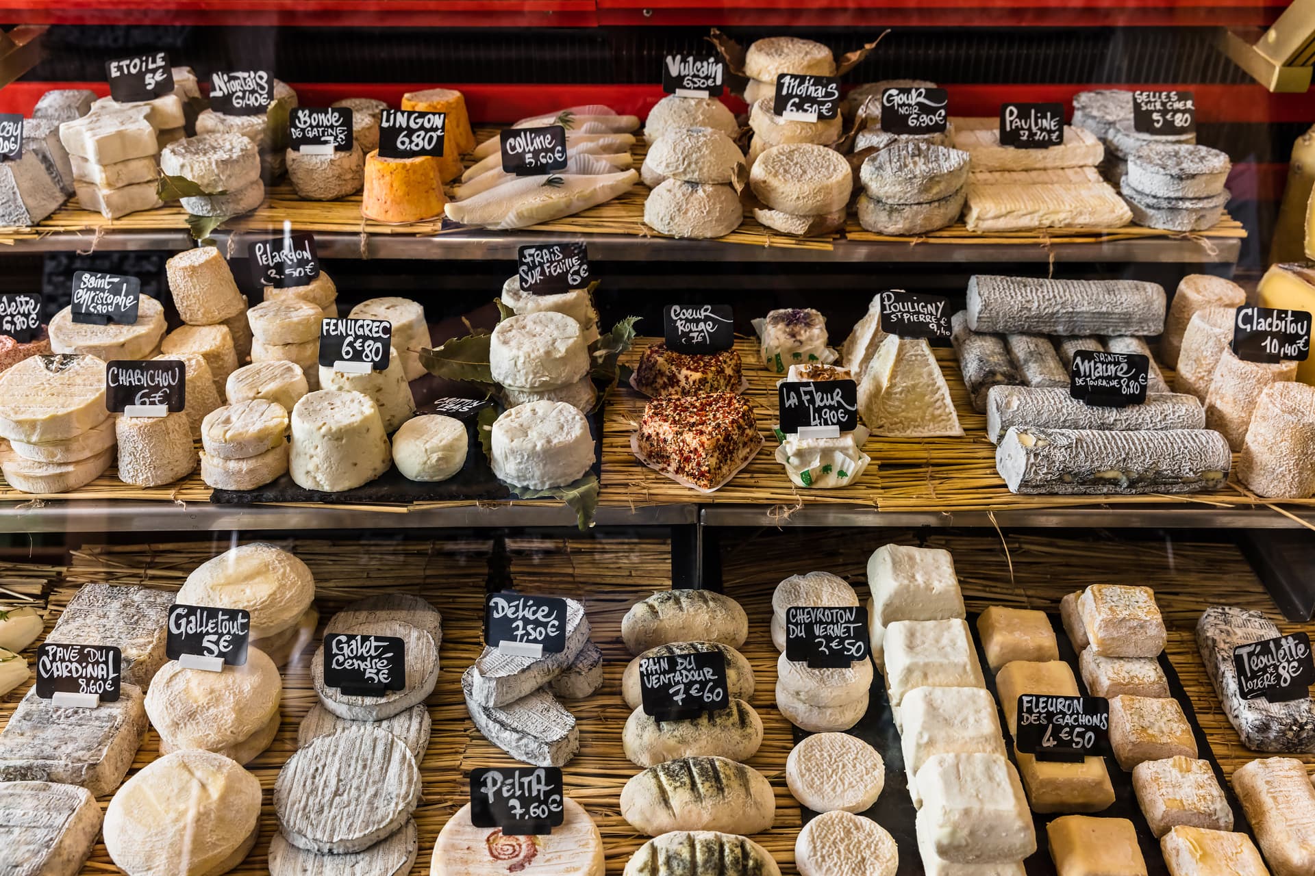 Different cheeses on display with handwritten price tags at a stall in the Aligre Market, Paris, France.